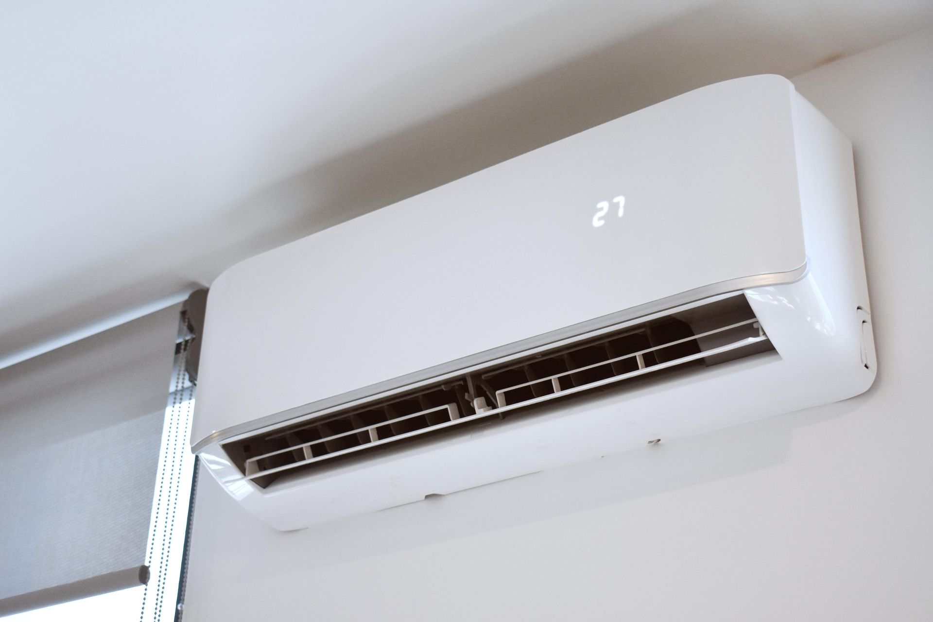 White air conditioner unit mounted on a white wall; digital display shows the number 27.