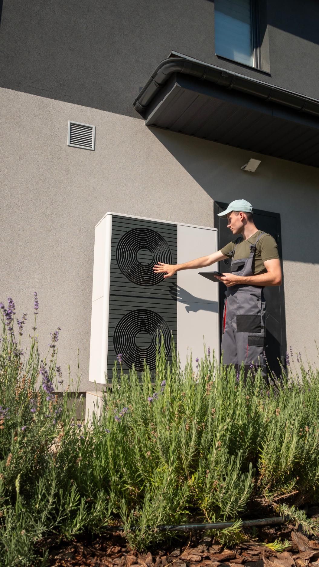 Air conditioning unit mounted on a white exterior wall next to a window.