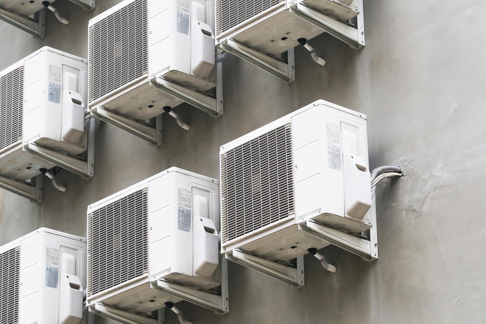 Several white air conditioning units mounted on a grey wall.