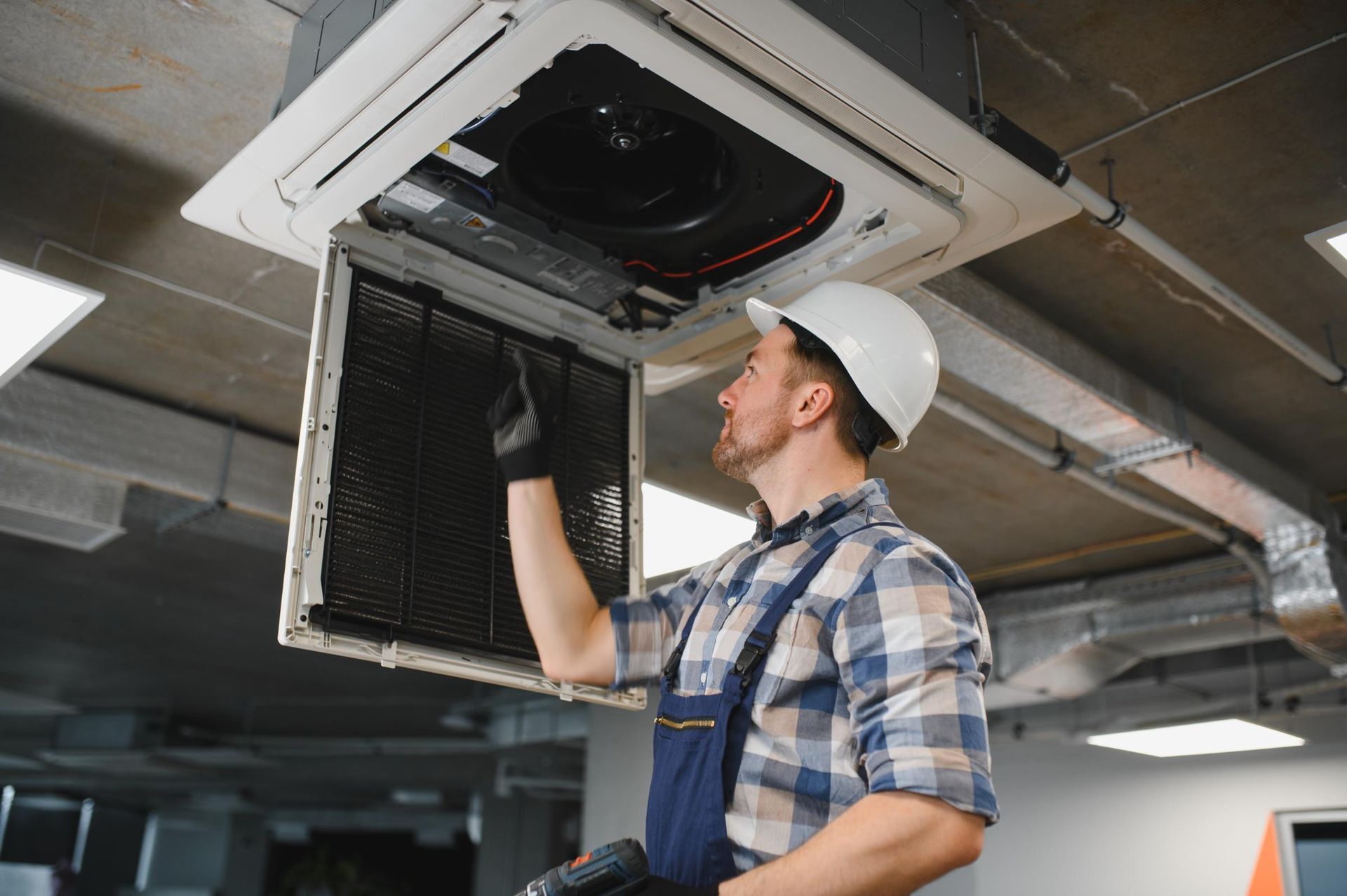 HVAC technician in a hard hat inspecting an air conditioning unit.