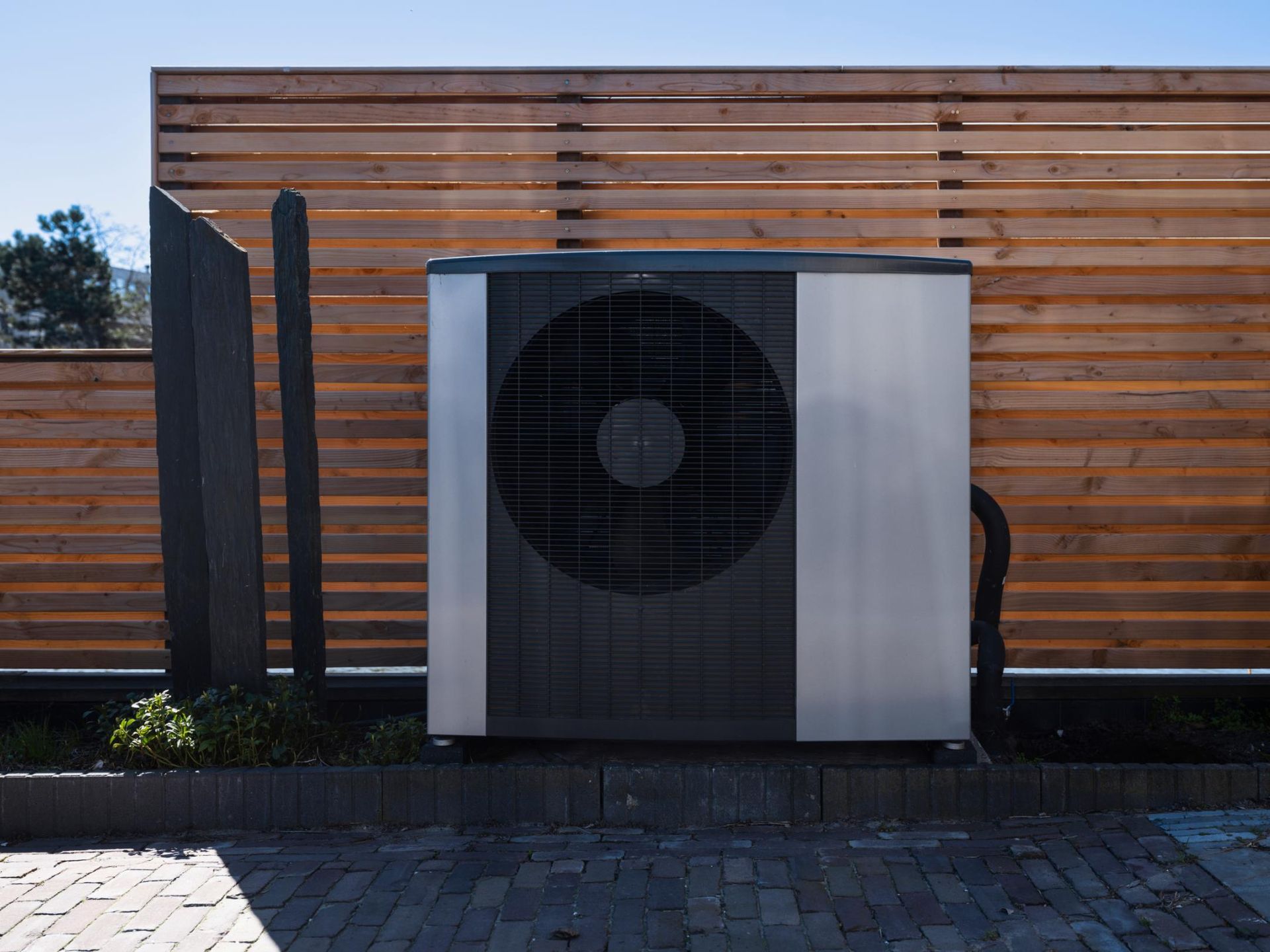 Heat pump unit next to wooden fence on a sunny day.