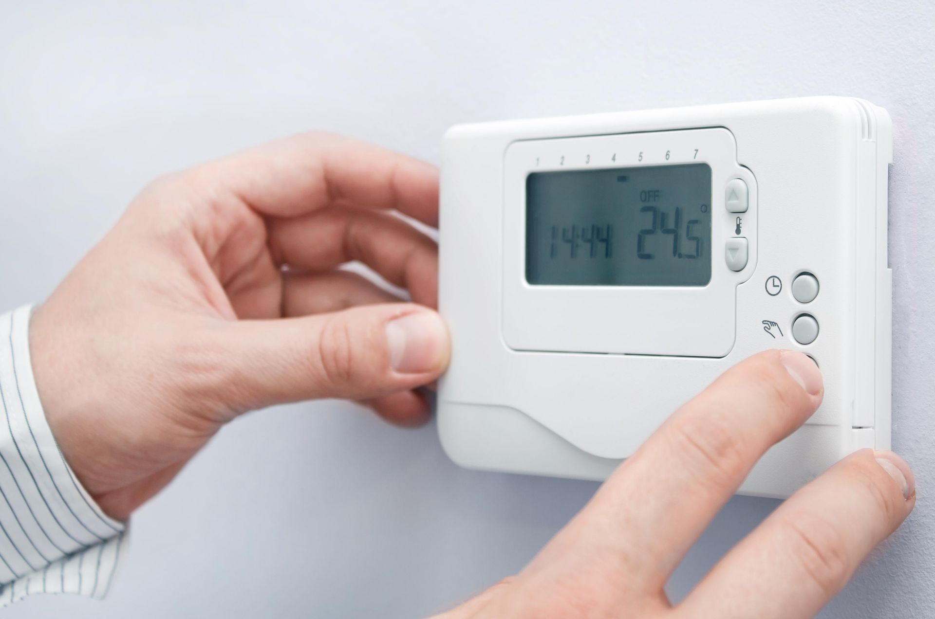 Person adjusting a white thermostat on a light gray wall.