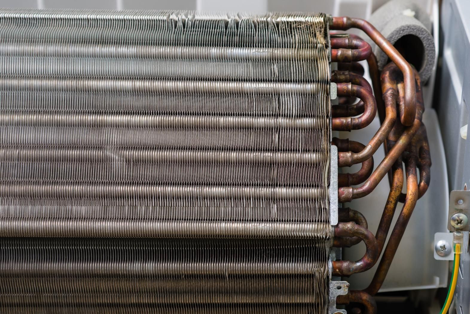 Close-up of a dirty air conditioner evaporator coil with copper tubing, showing a buildup of dust and debris.