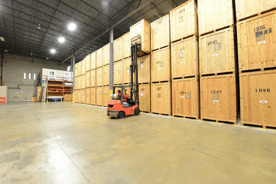 A forklift is driving through a large warehouse filled with wooden crates.