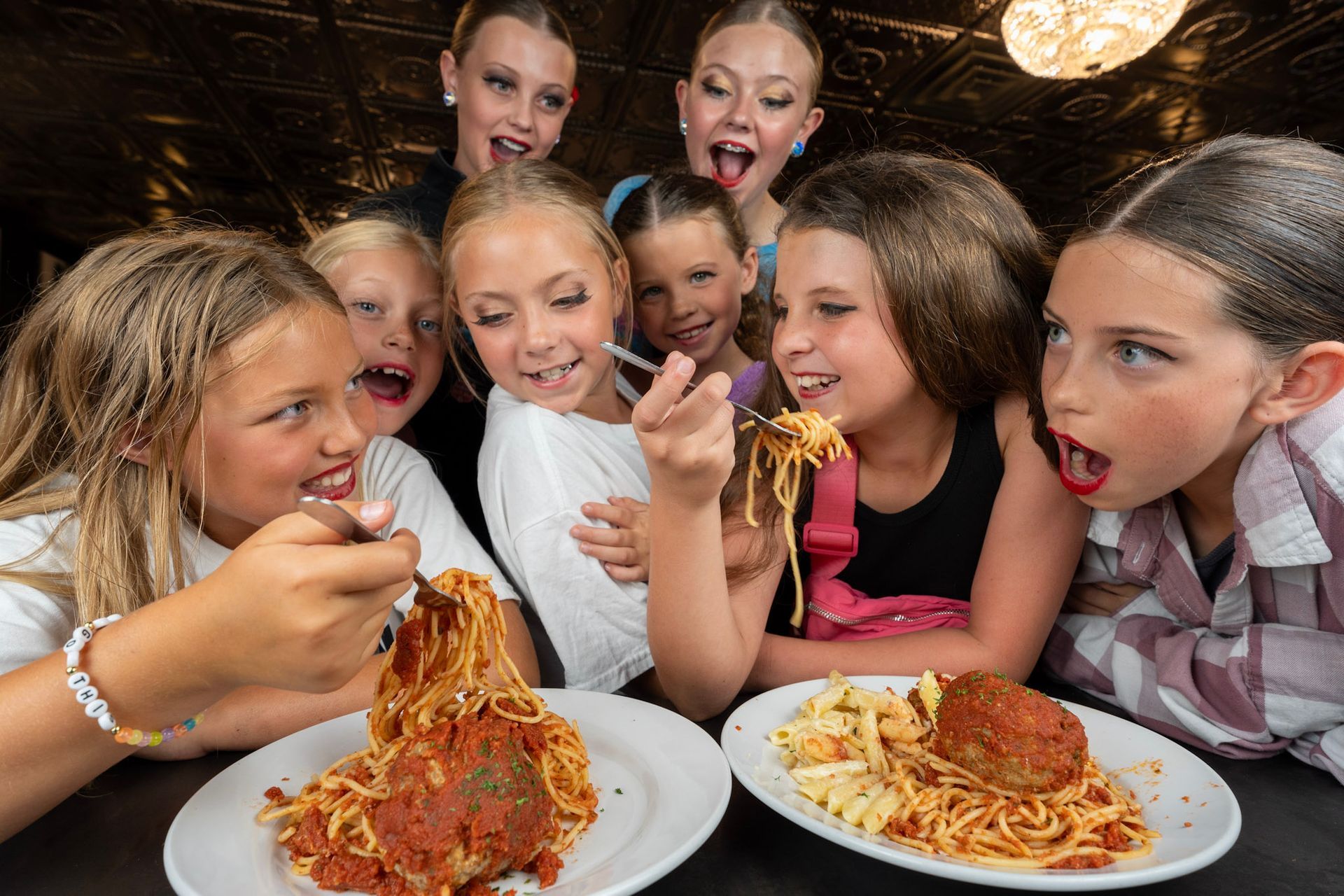 A group of young girls are eating spaghetti and meatballs at a restaurant.