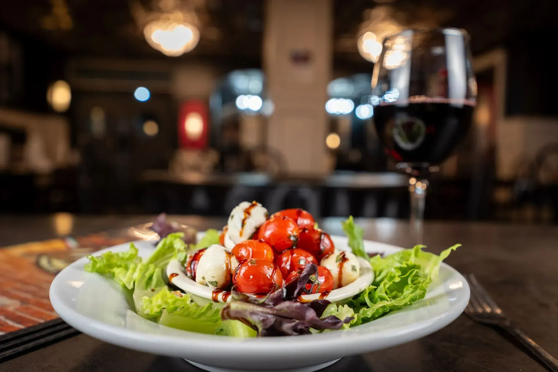 A salad on a plate with a glass of wine in the background.