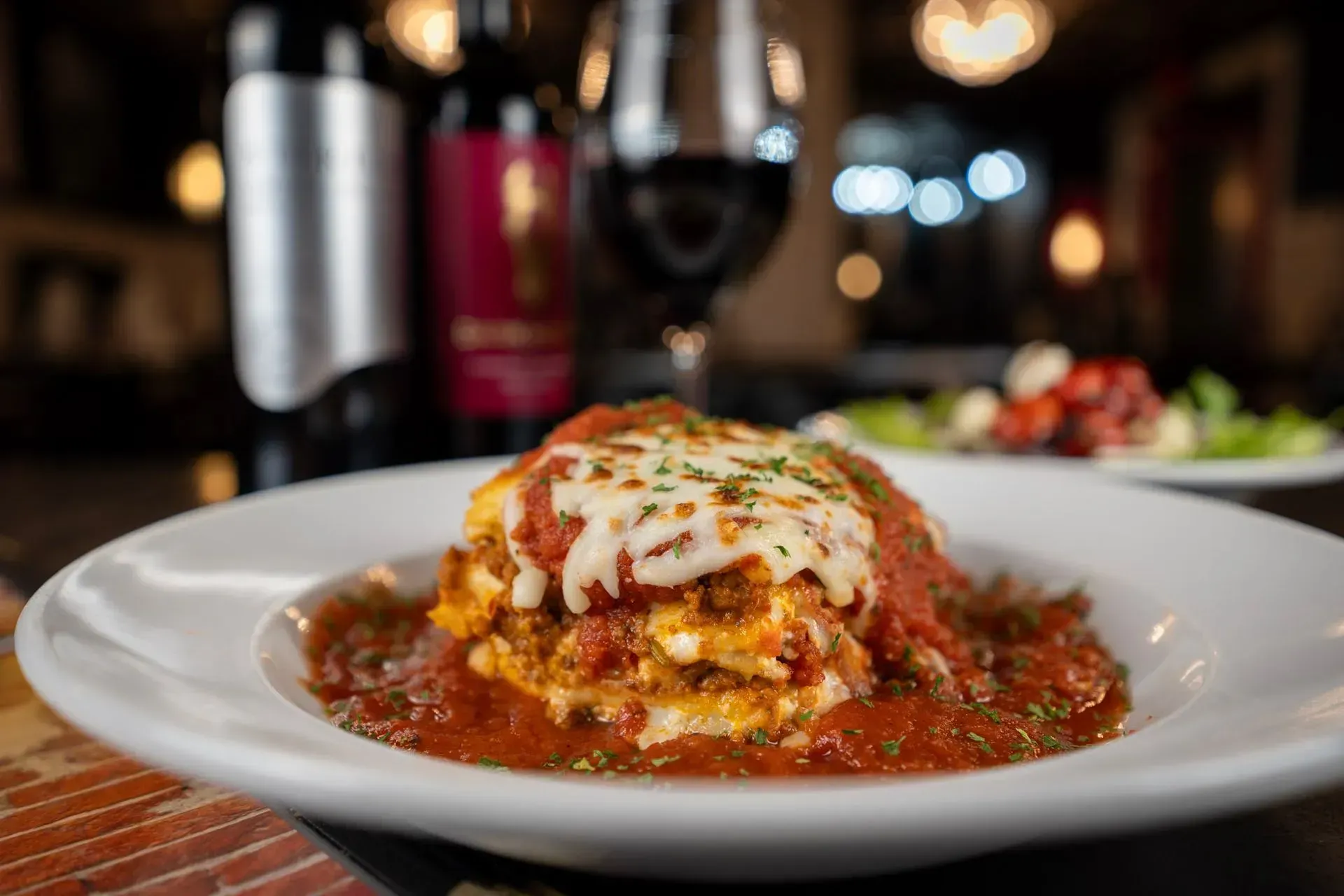 A white plate topped with a lasagna and a glass of wine on a table.