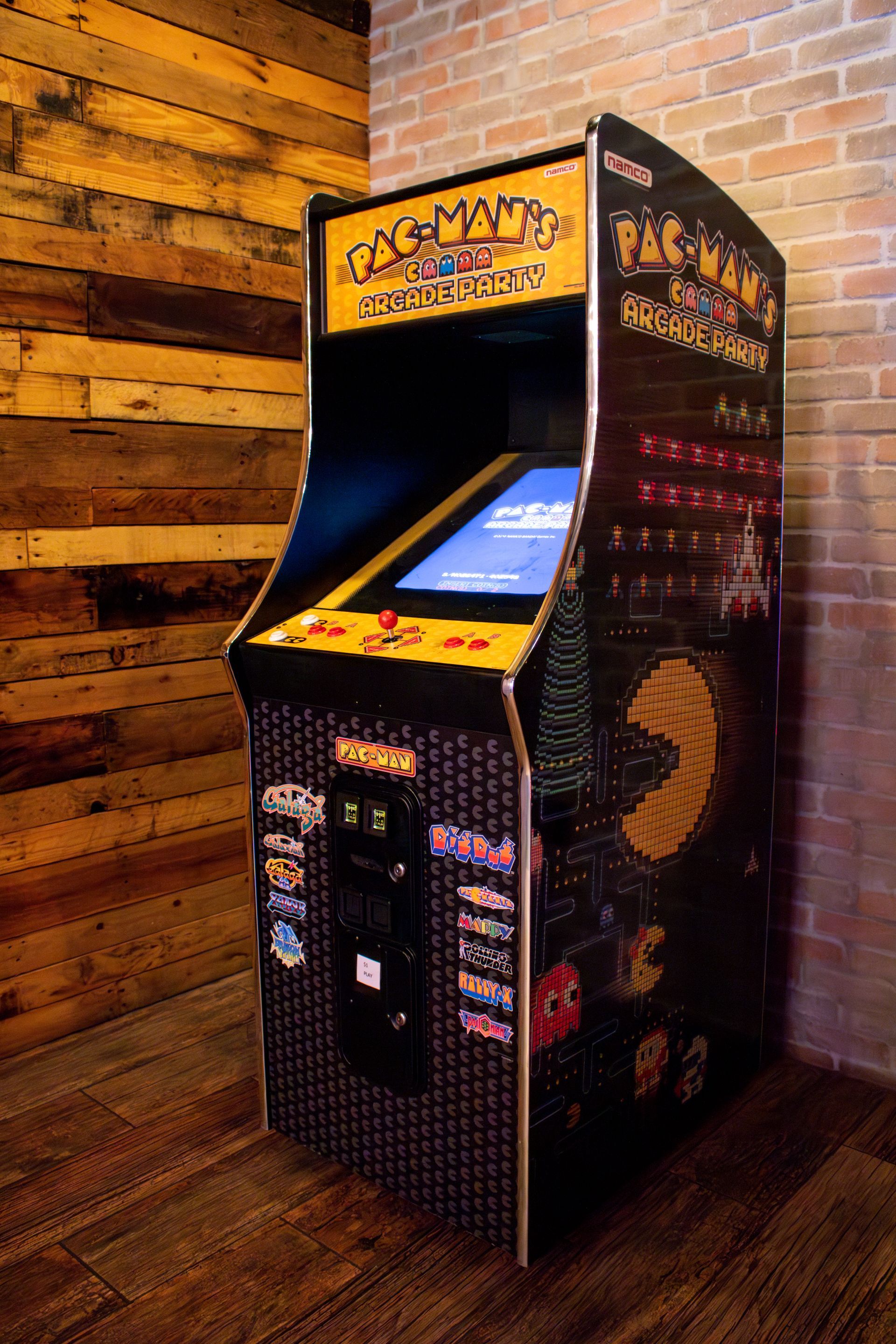 A pac man arcade game is sitting in a corner of a room next to a brick wall.