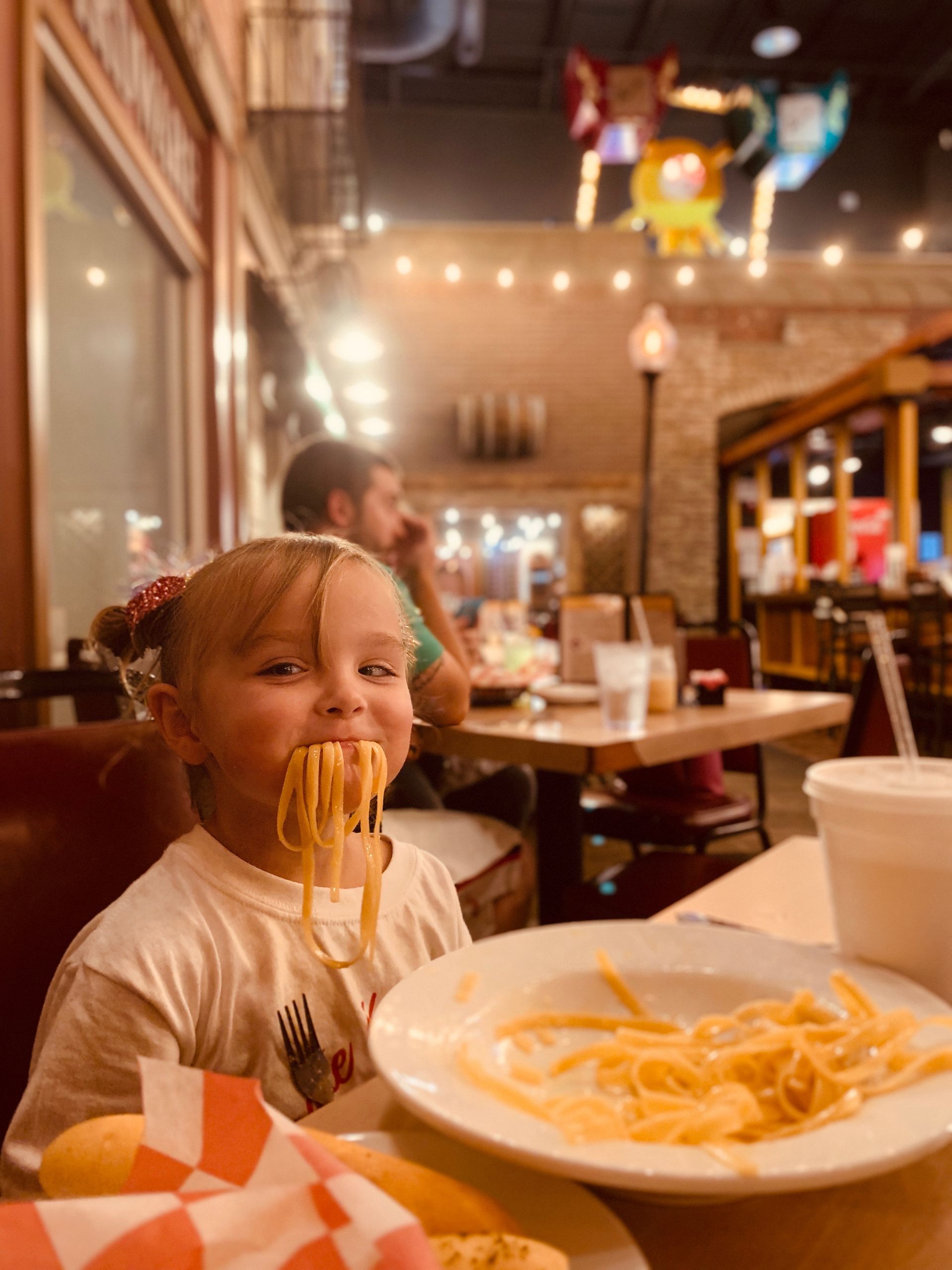 A little girl is eating spaghetti at a restaurant.