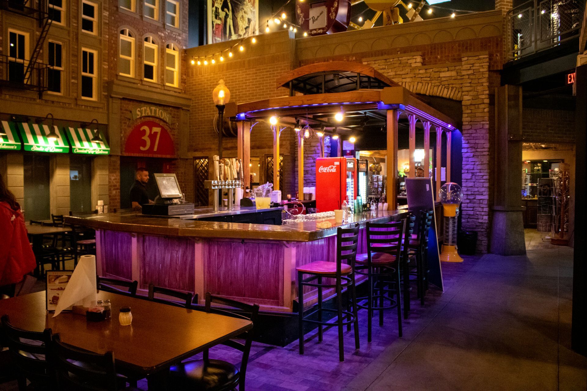 A restaurant with tables and chairs and a bar with purple lights.