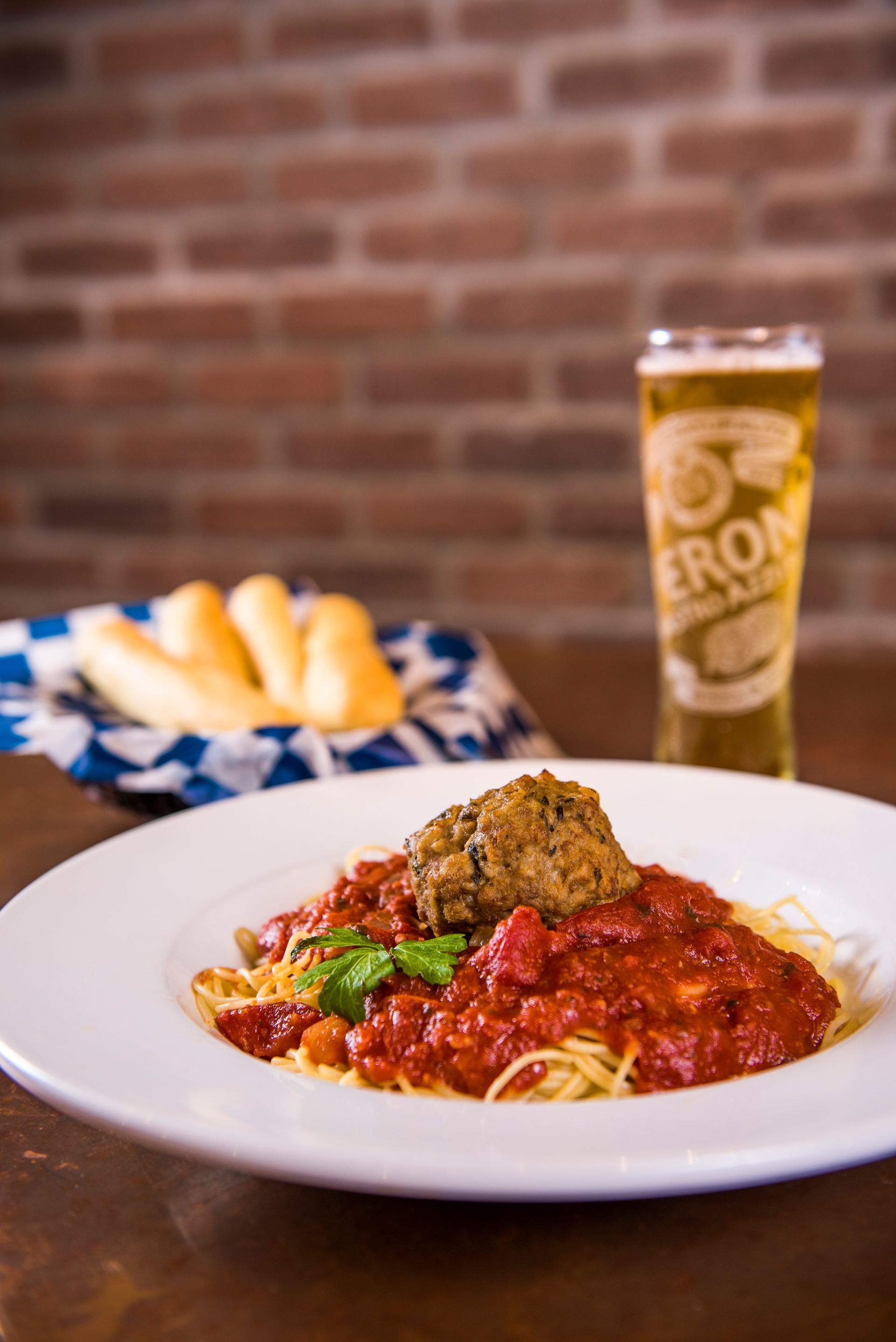 A plate of spaghetti and meatballs with a glass of beer in the background.