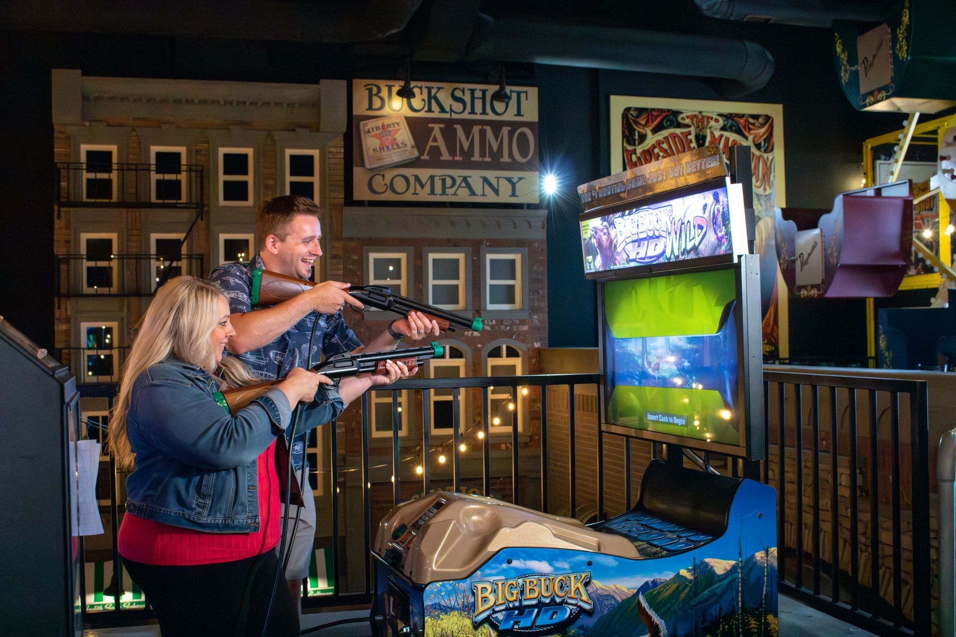 A man and a woman are playing a video game in an amusement park.
