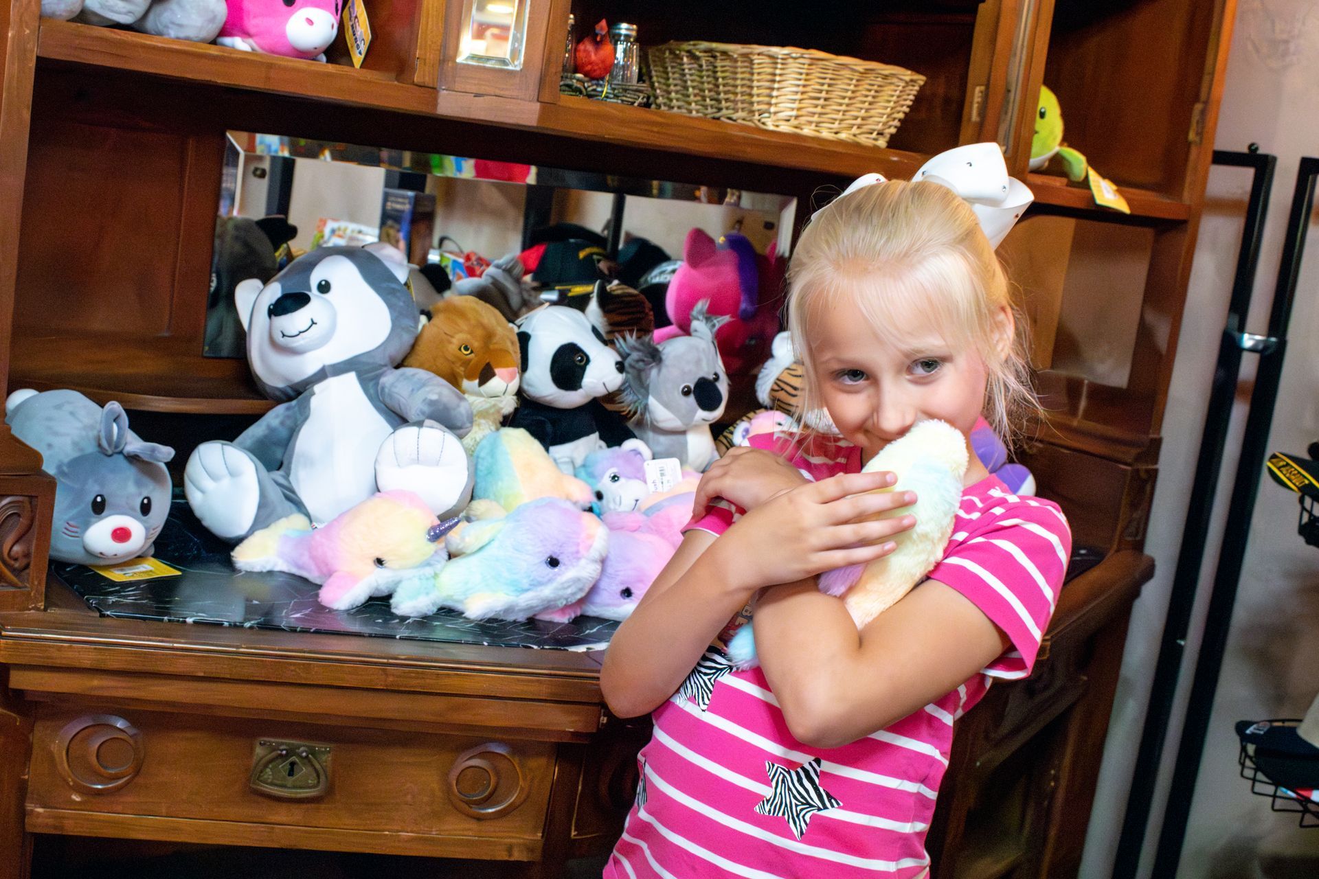 A little girl holding a stuffed animal in front of a shelf full of stuffed animals