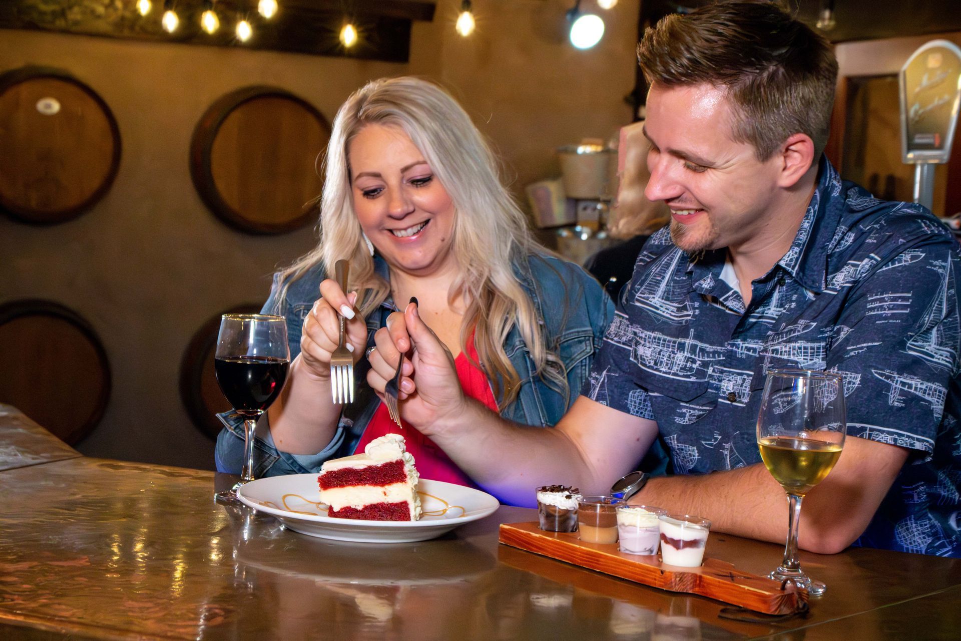 A man and a woman are sitting at a bar eating cake and drinking wine.