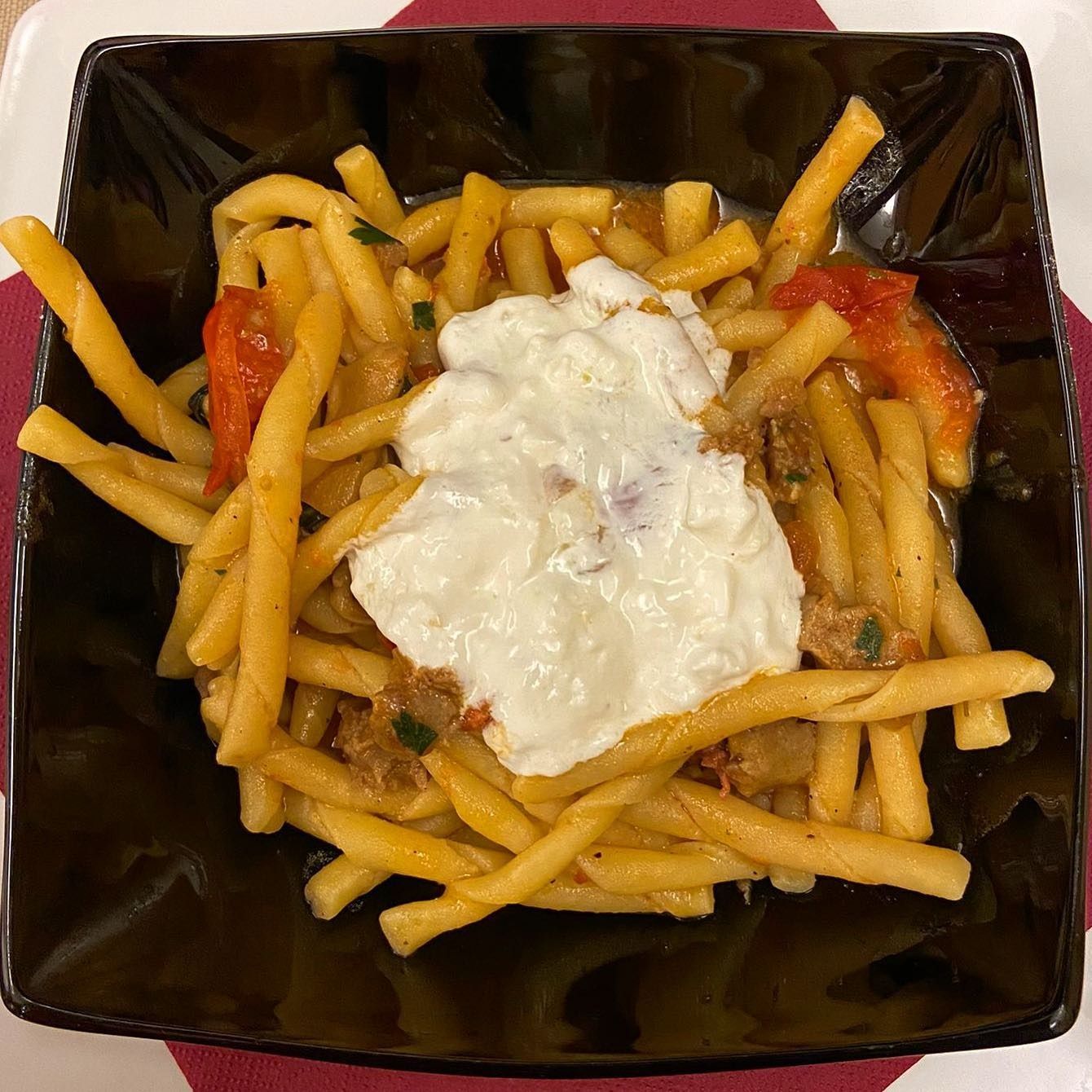 Piatto di pasta con pomodori e salsa bianca cremosa in una ciotola nera.