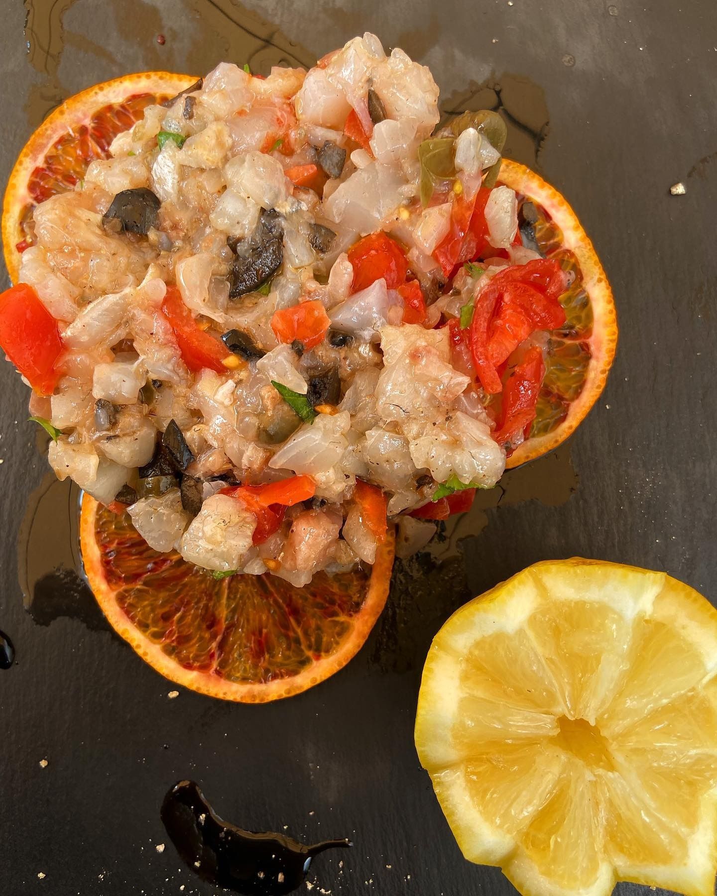 Piatto di frutti di mare su fette d'arancia e spicchi di limone. Contiene frutti di mare tritati, pomodori, olive e capperi.
