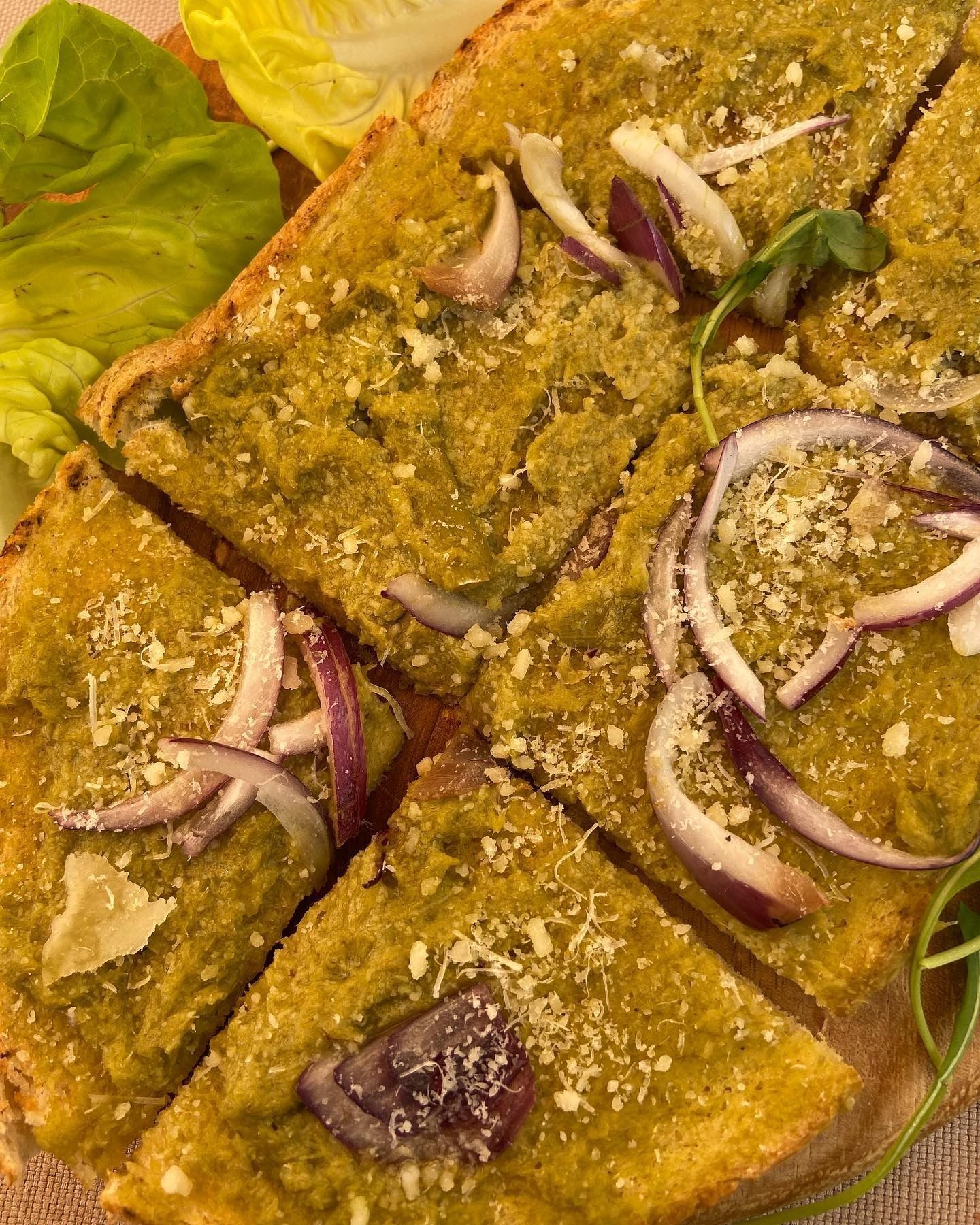 Fette di pane piatto condite con pesto verde, cipolla rossa e formaggio grattugiato.