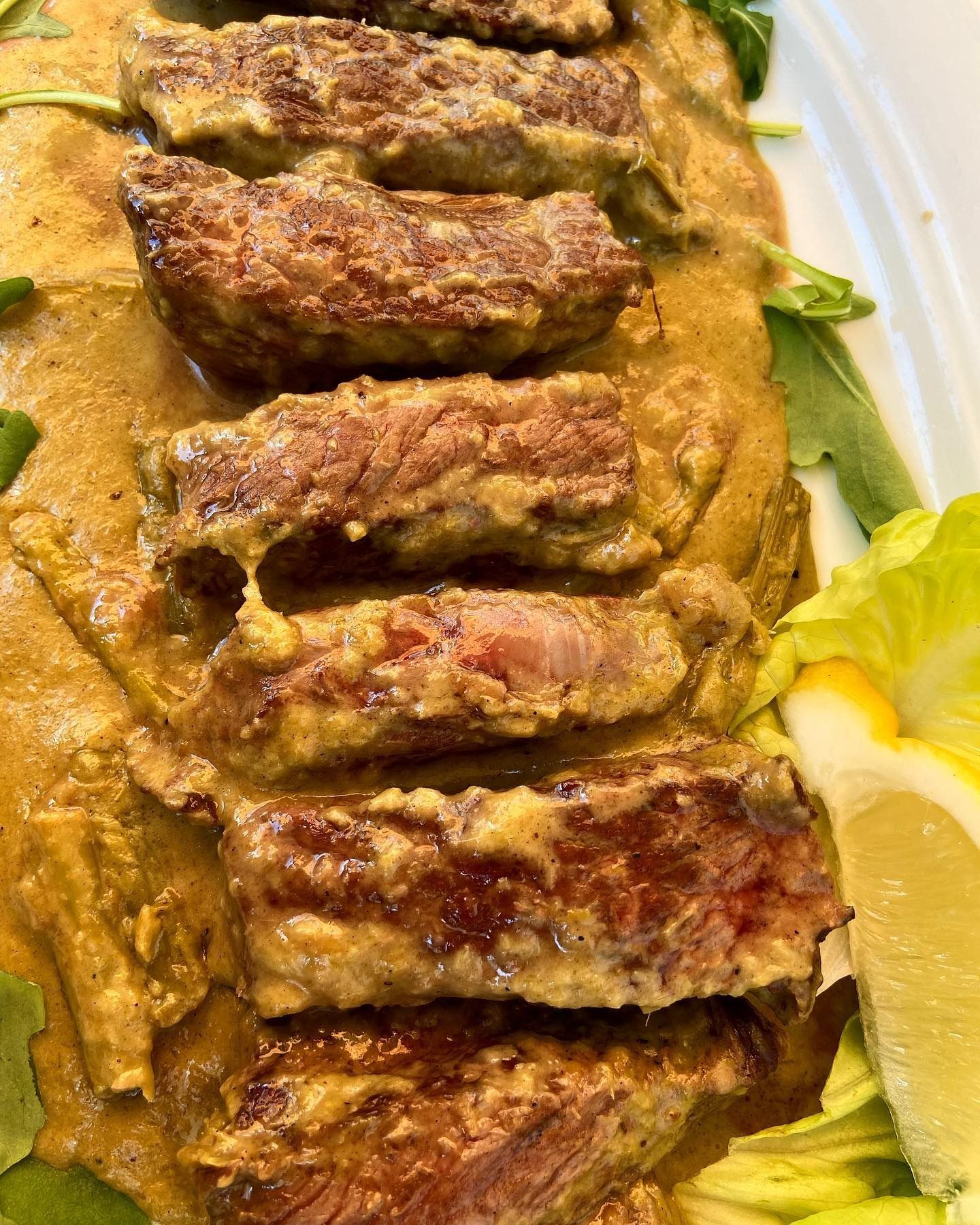 Bistecca tagliata a fette con salsa cremosa, guarnita con verdure e spicchio di limone.