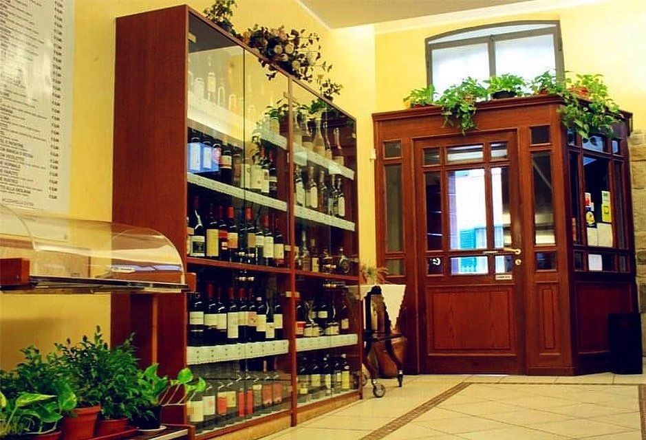 Ingresso del ristorante con porta in legno, espositore per vini, piante in vaso e pareti beige.