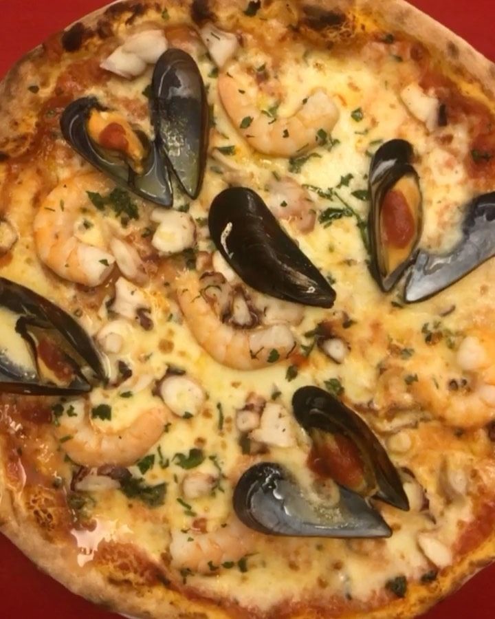 Pizza ai frutti di mare con cozze e gamberi su una superficie rossa.