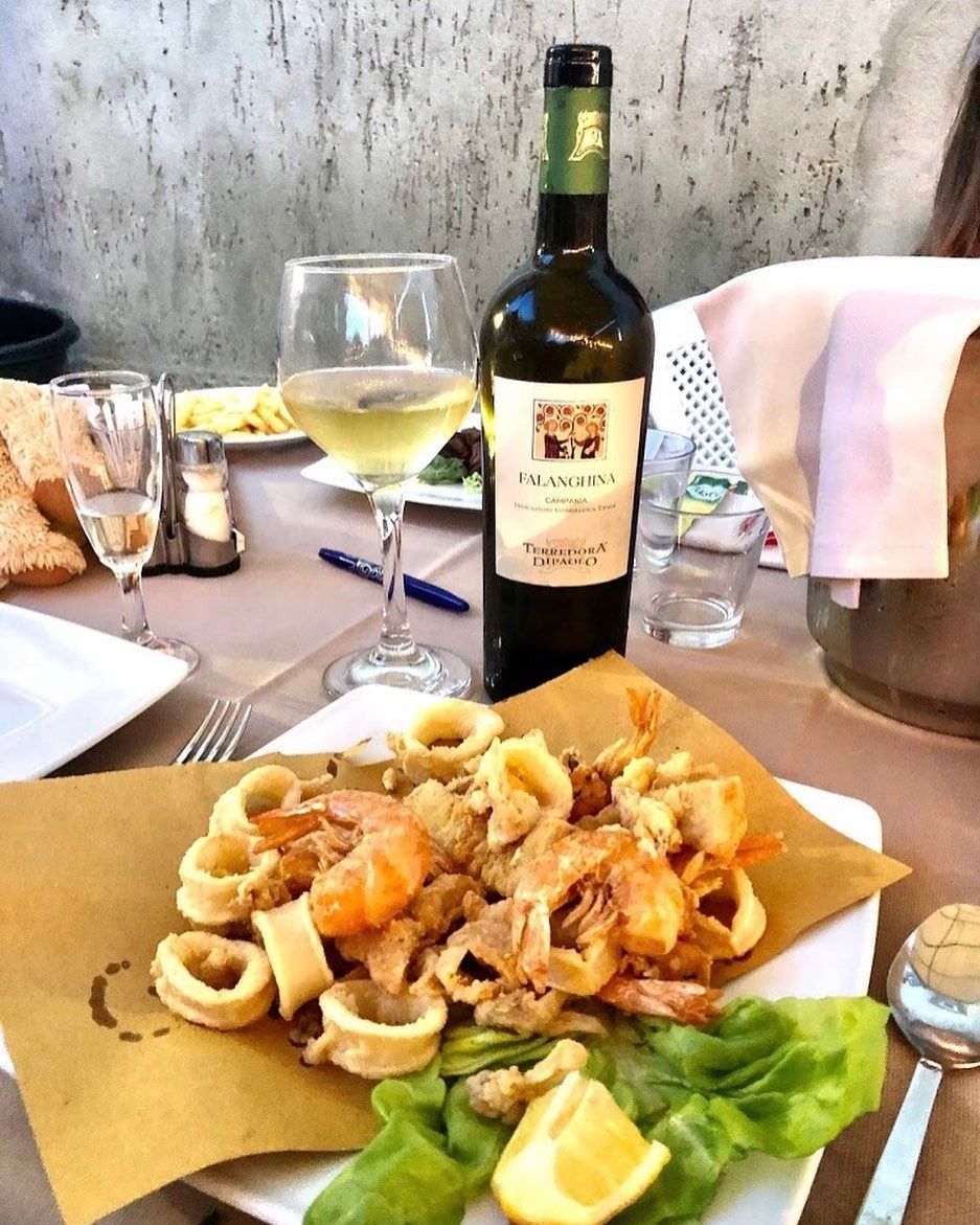 Piatto di pesce fritto, vino bianco e bottiglia su un tavolo con una tovaglia bianca e un bicchiere.