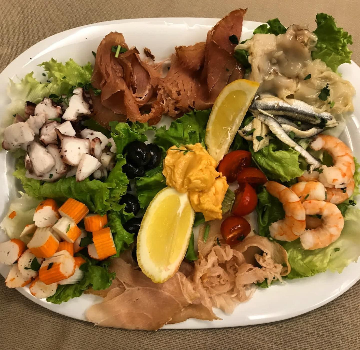 Piatto di frutti di mare con polpo, gamberi, prosciutto, olive, limone e pomodori su lattuga.