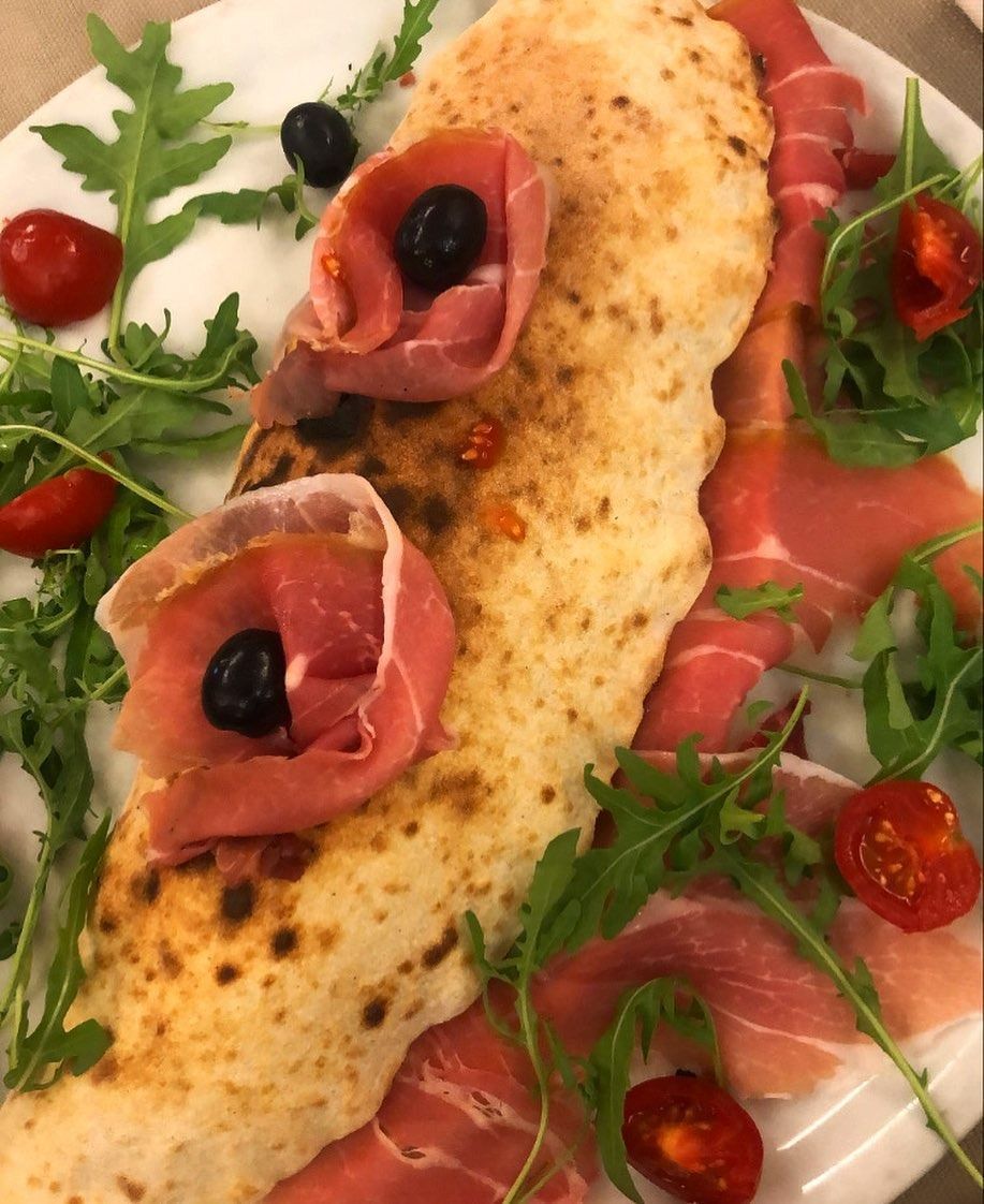 Calzone di pizza con prosciutto e rucola, guarnito con pomodori e olive.