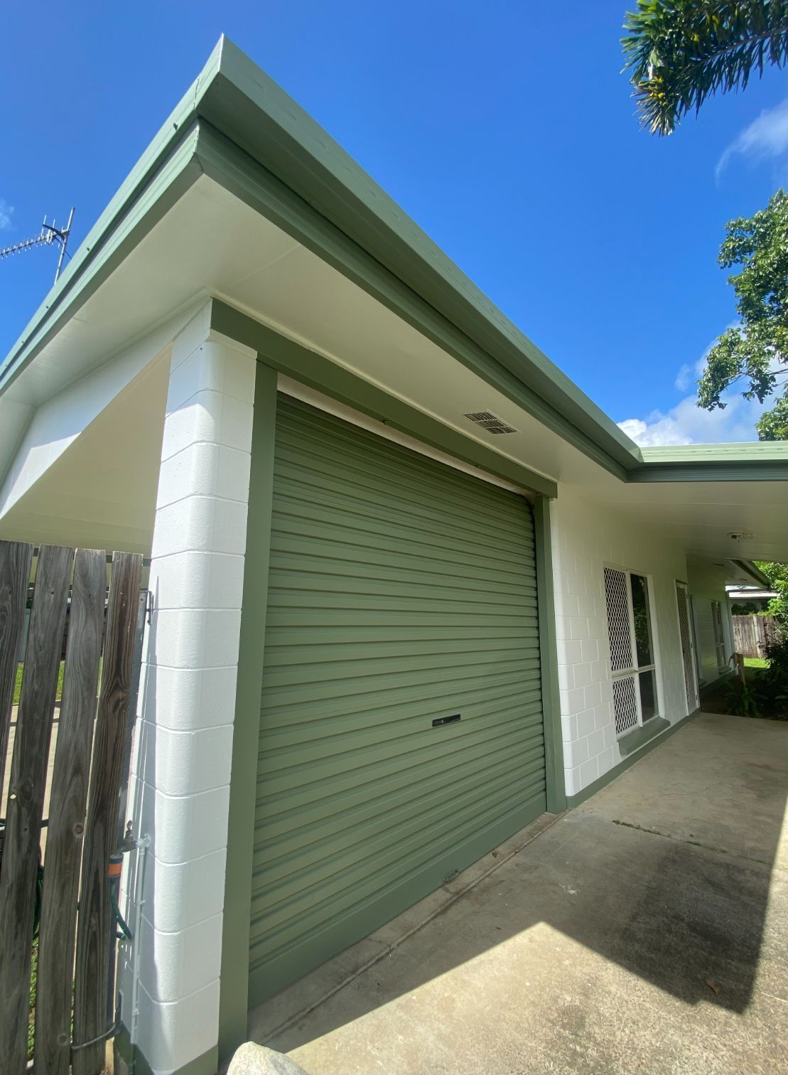 A White House with A Green Garage Door and A Palm Tree in Front of It — Painting & Maintenance FNQ Handyman Service in Clifton Beach, QLD