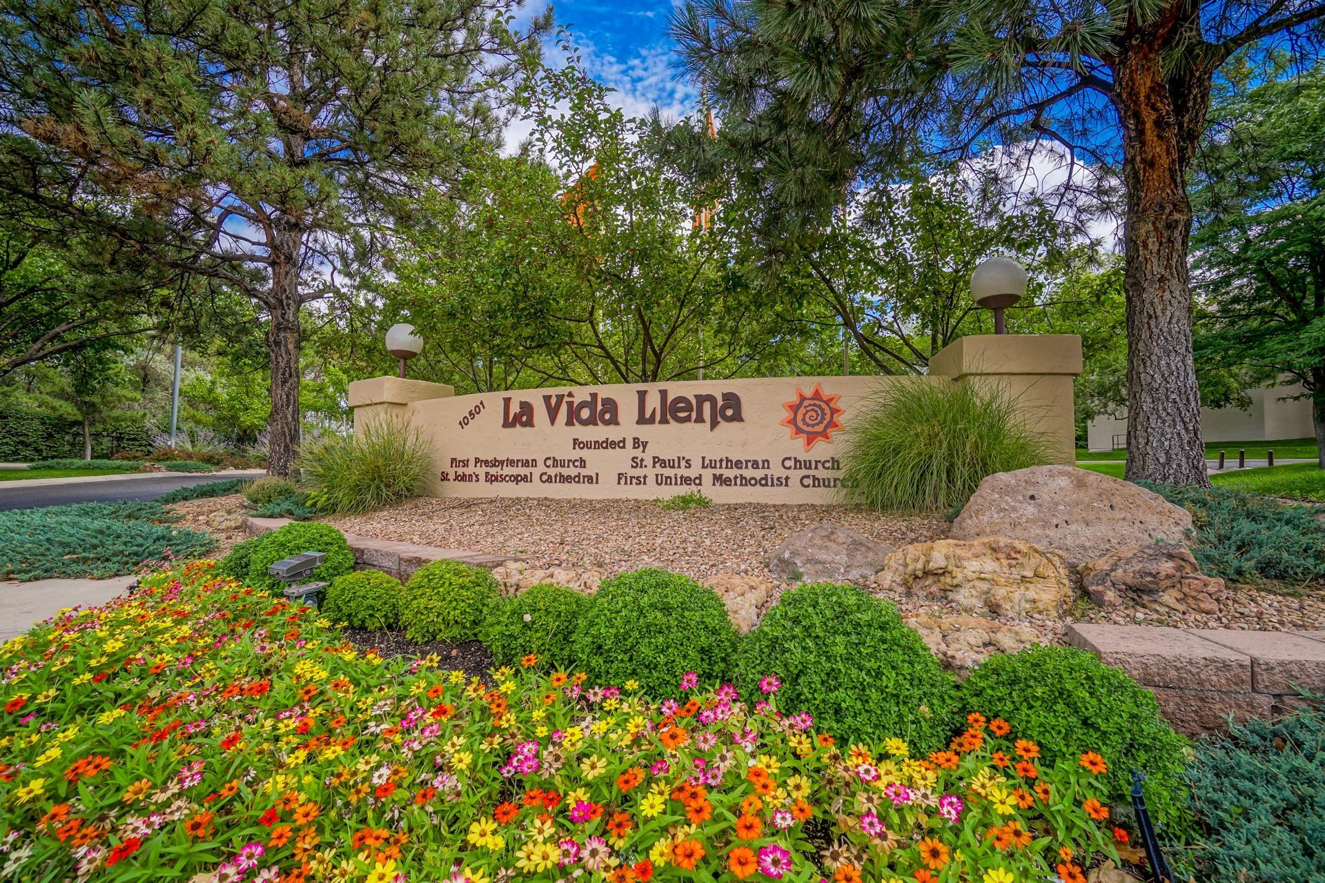 a sign for la vida llena is surrounded by flowers and trees .