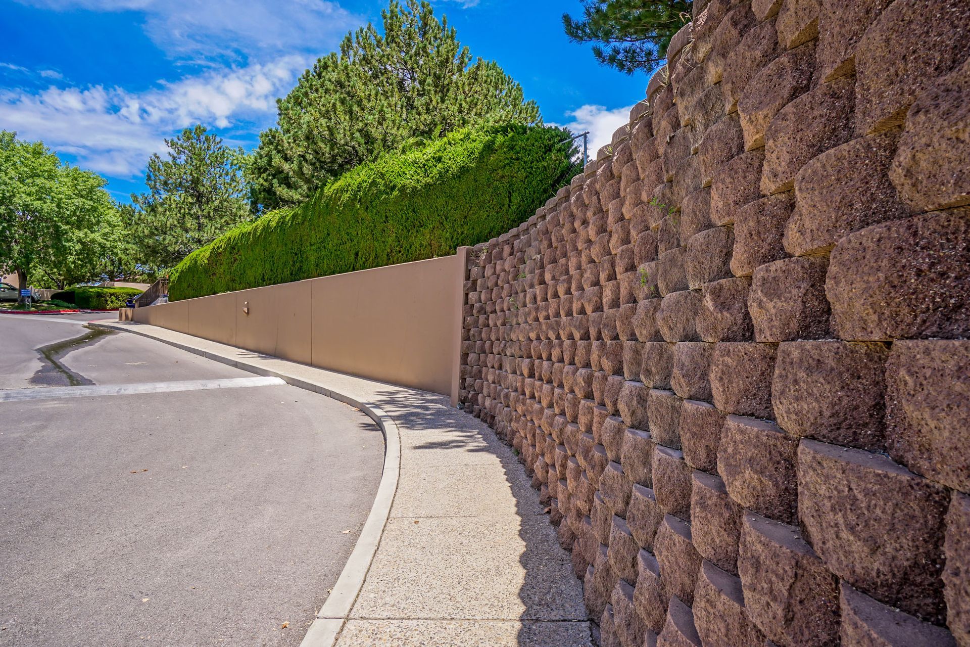 a stone wall along the side of a road next to a sidewalk .