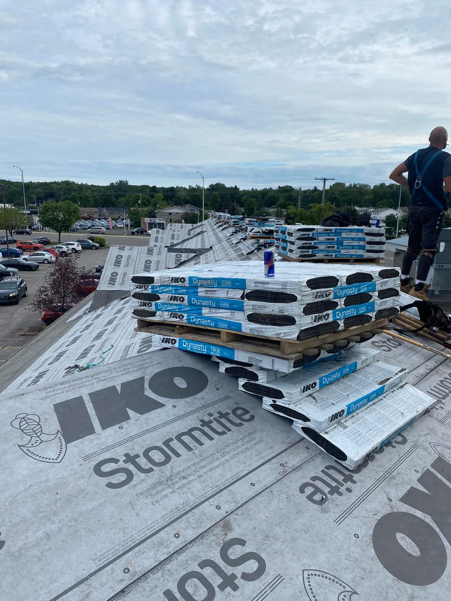 Un homme se tient debout sur un toit avec une pile de matériaux de toiture.