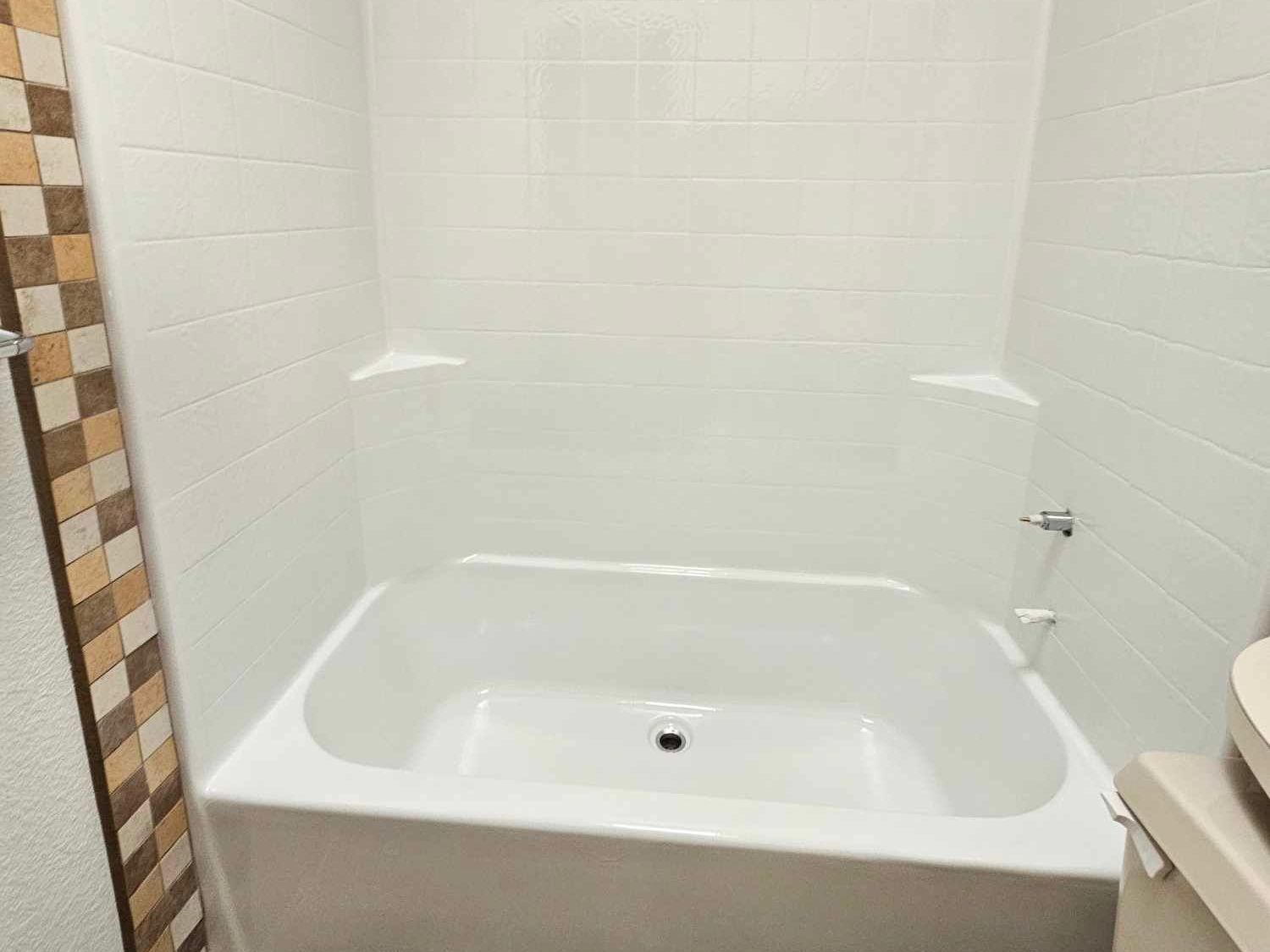 Image of a bathtub that has been restored using bathtub refinishing. You can see all white bathtub with white tile bathroom wall.