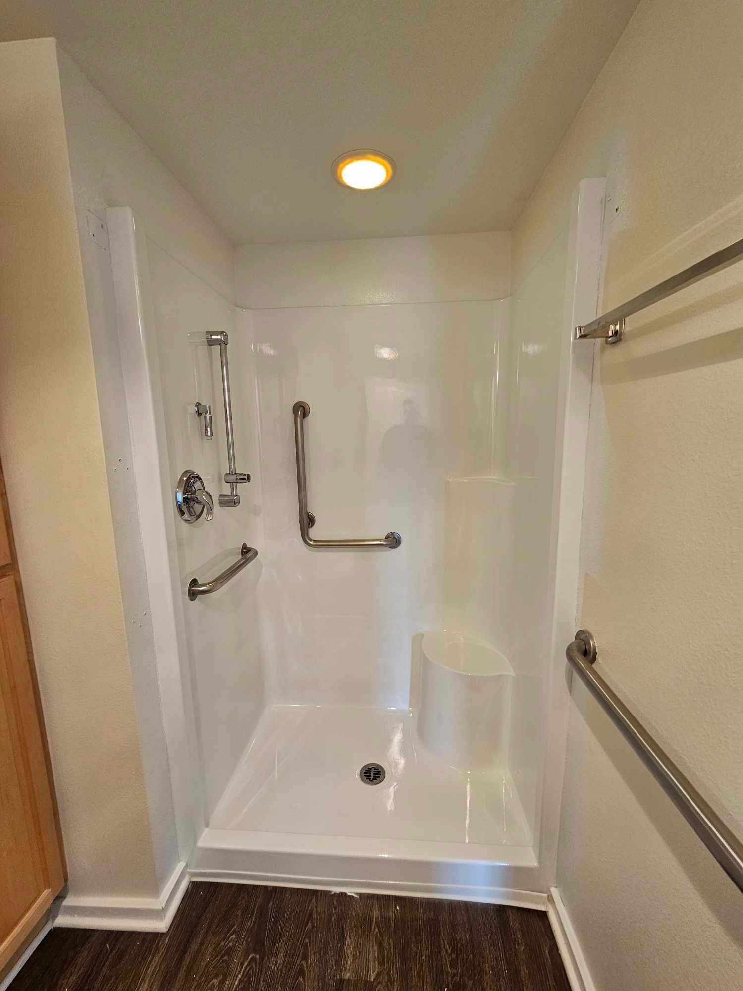 Picture of a shower that has been restored using shower refinishing services. You can see a zoomed out picutre of a white tile shower with metal rails.