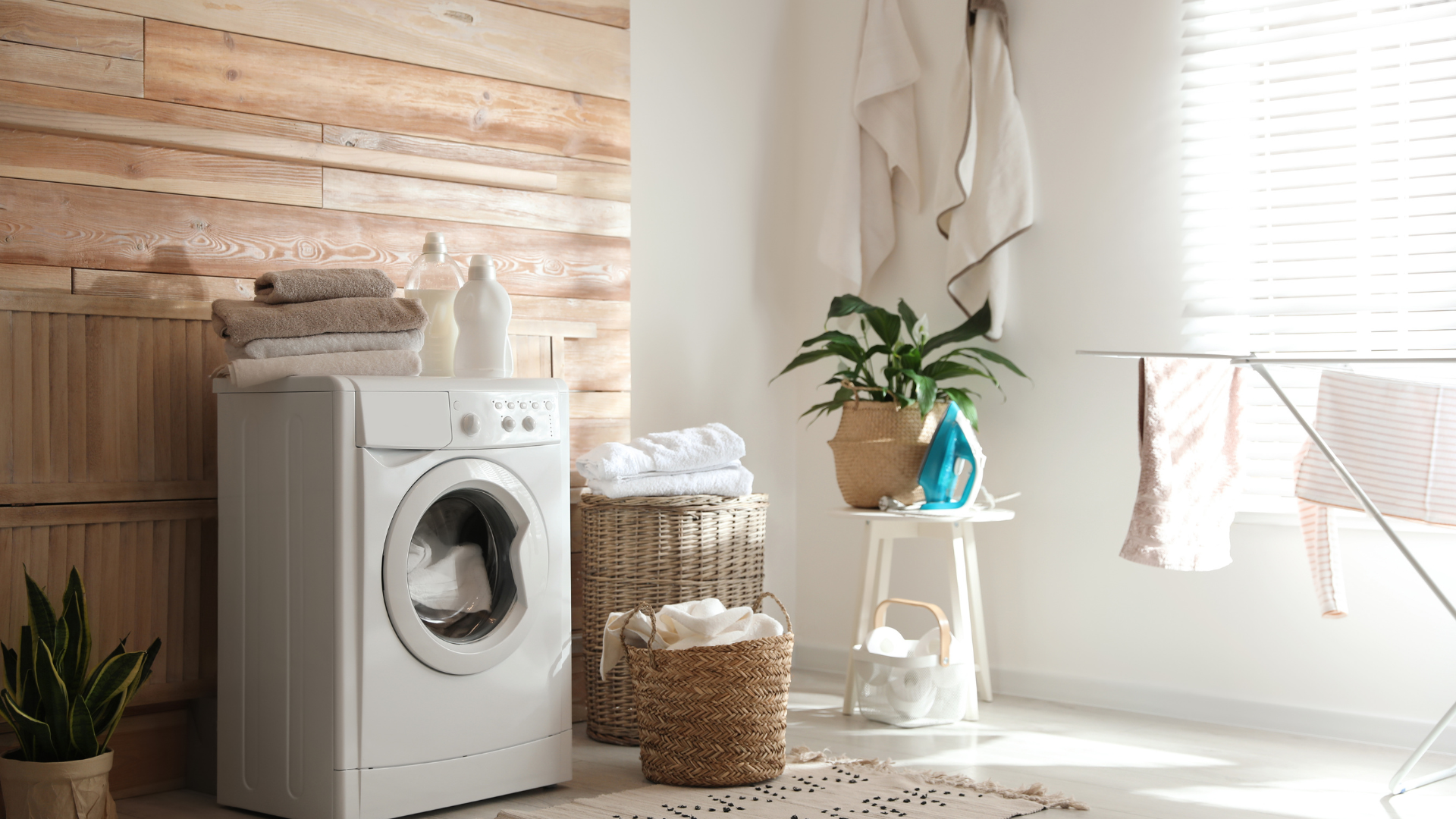 Laundry room with washing machine, laundry basket, drying rack, towels, and plants.