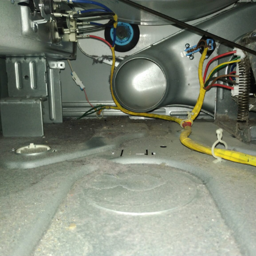 Interior view of a dryer with electrical wiring, vent, and lint accumulation on the floor.