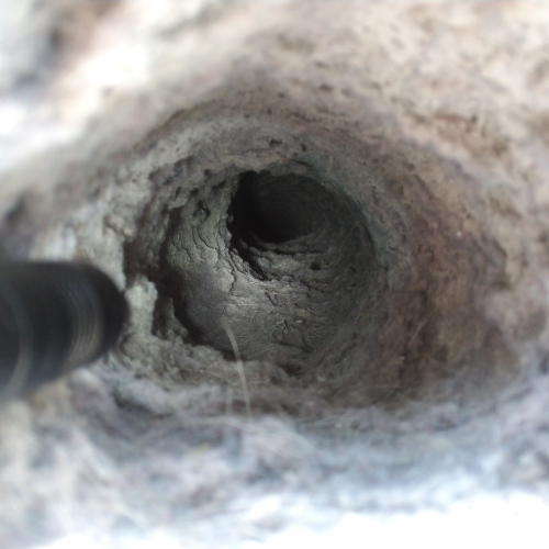 Looking inside a gray, textured hole, possibly a chimney. A dark tool extends into it.