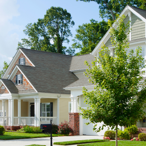Two-story house with tan siding, brick accents, and a tree in the front yard.
