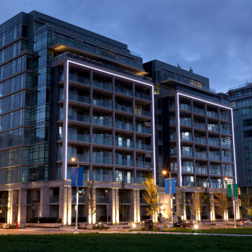 Modern glass condo building with illuminated edges at dusk.
