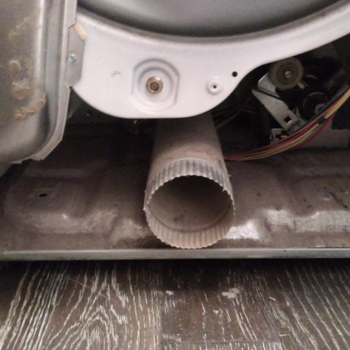 Dryer vent, close-up view: metal vent tube with lint buildup, beneath the dryer drum.