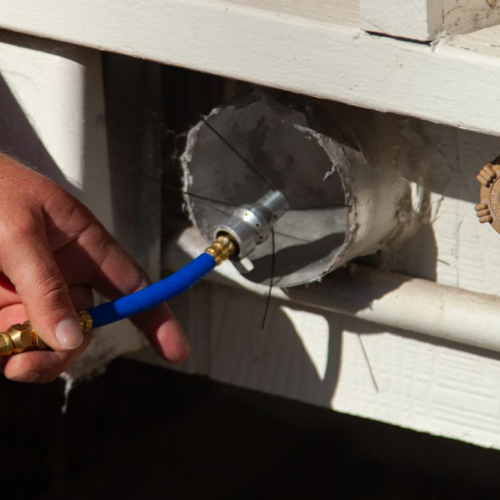 Hand holding blue hose connected to fitting in a white-walled, cylindrical opening.