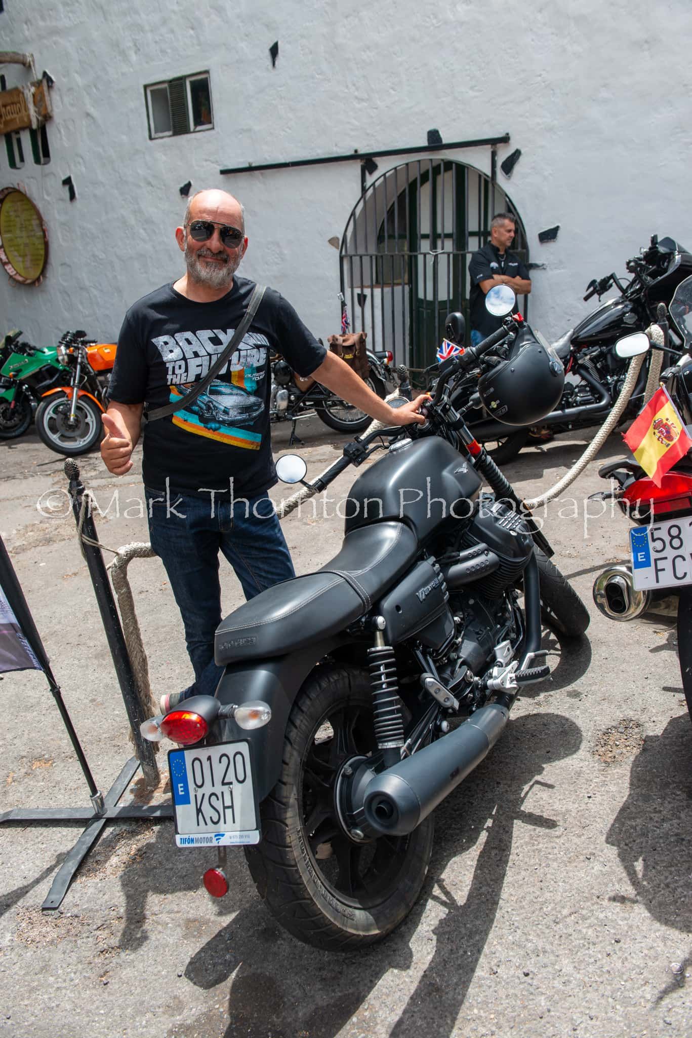 A man is standing next to a black motorcycle.