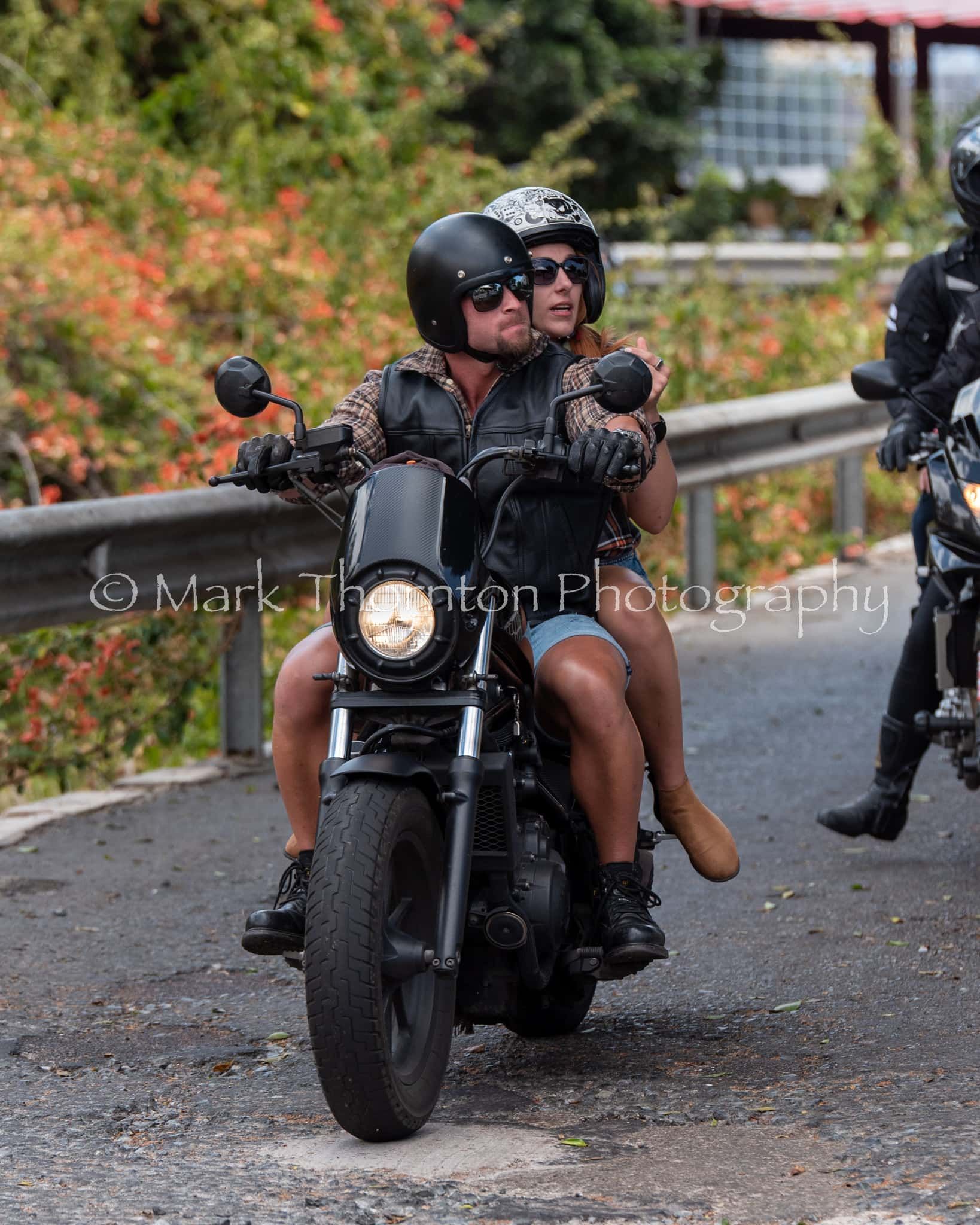 A man and a woman are riding a motorcycle down a road.
