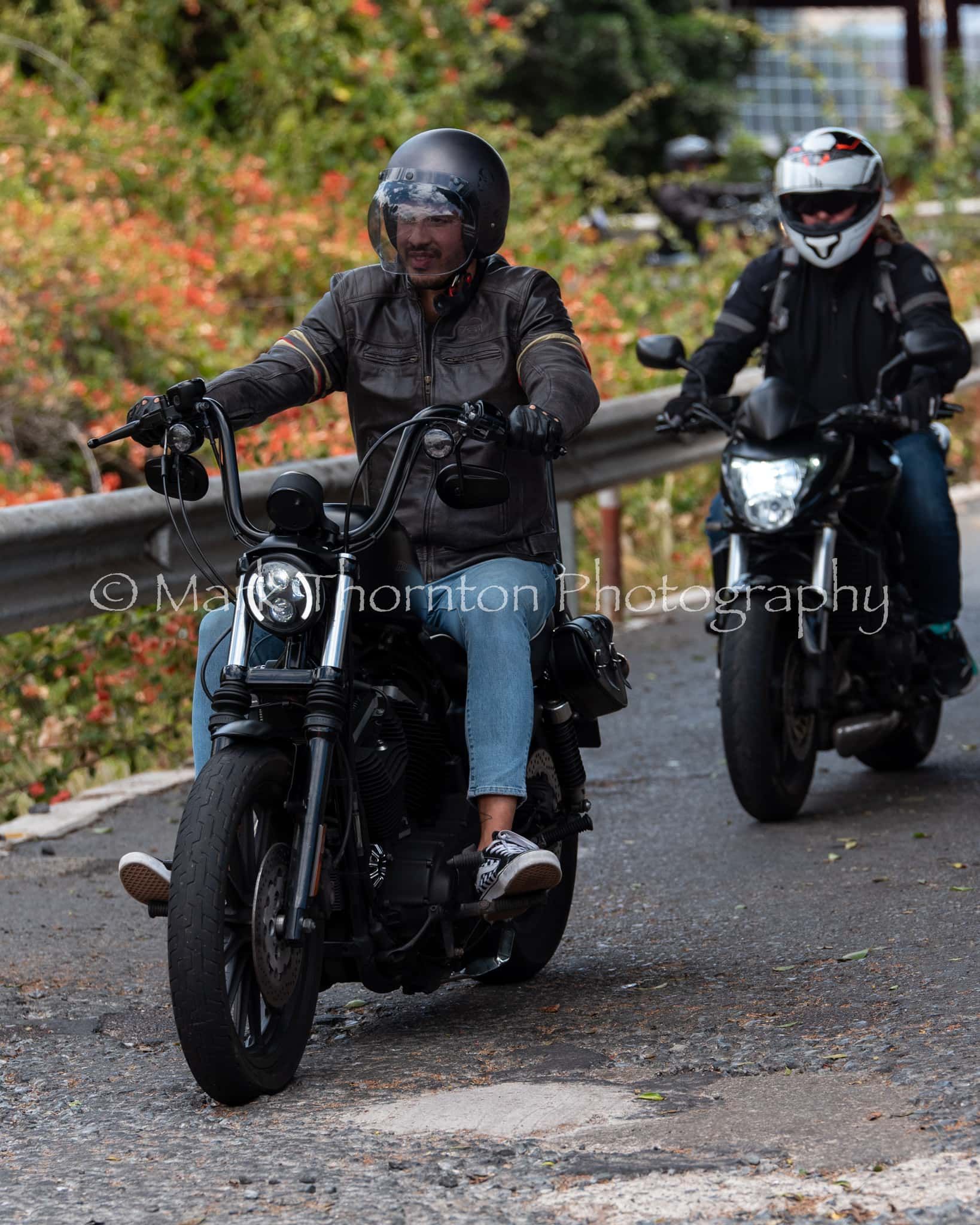 Two men are riding motorcycles down a road.