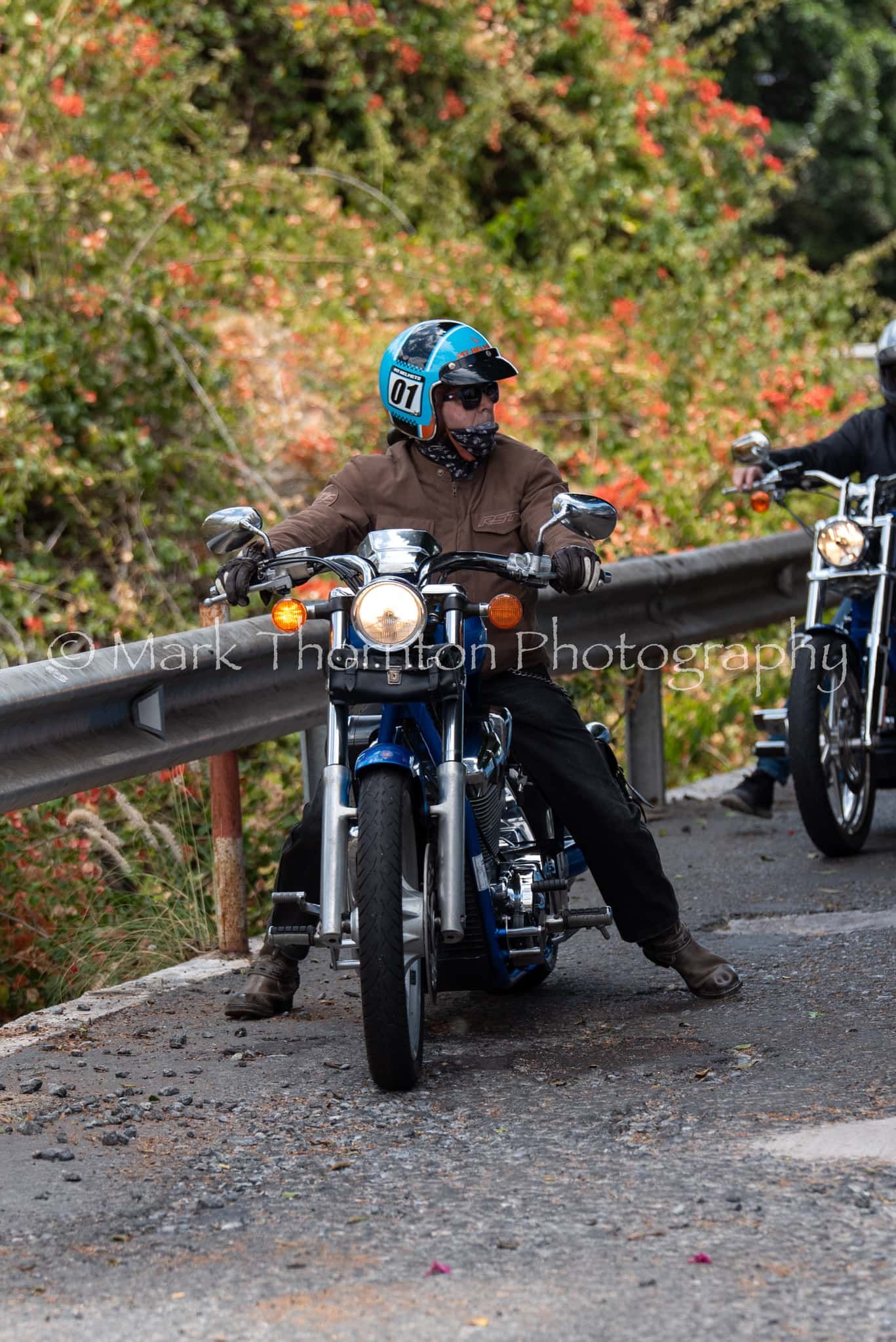 A man wearing a blue helmet is riding a motorcycle down a road.