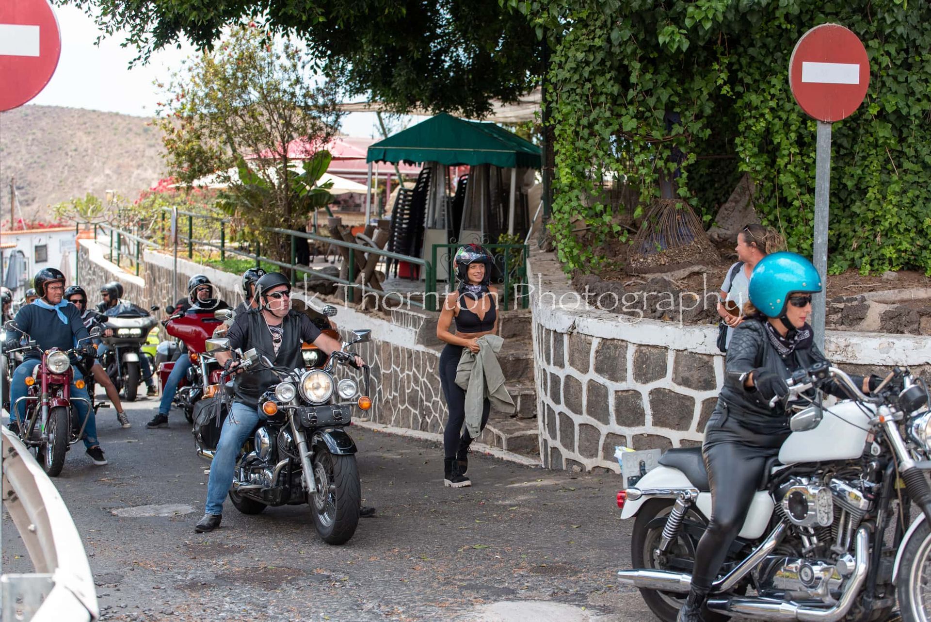 A group of people riding motorcycles on a street with a no entry sign