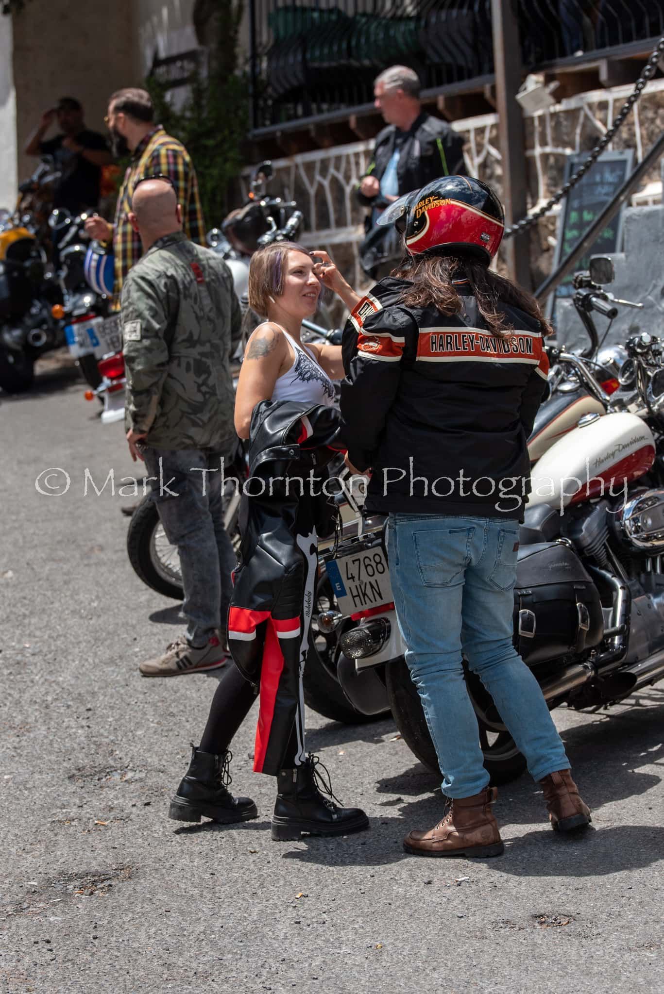 A group of people are standing around motorcycles on a street.