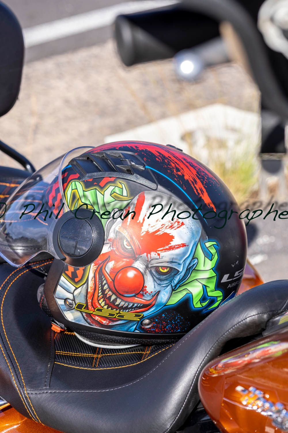 A motorcycle helmet with a clown on it is sitting on the seat of a motorcycle.