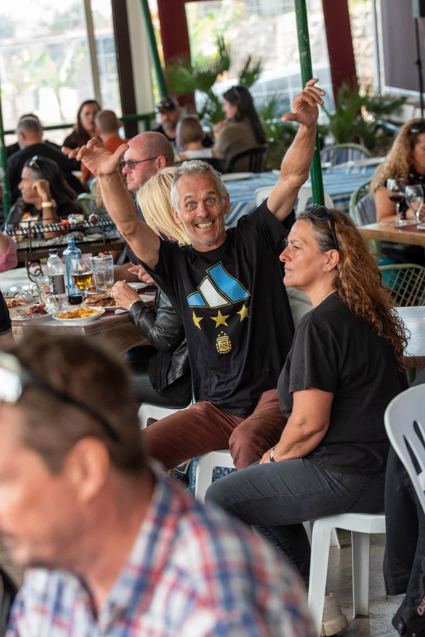 A group of people are sitting at tables in a restaurant with their arms in the air.