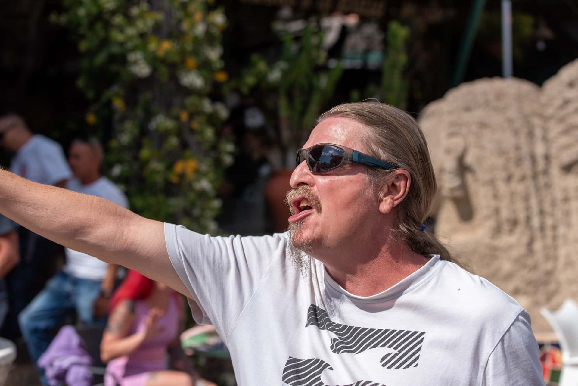 A man wearing sunglasses and a white shirt is standing in front of a sand sculpture.