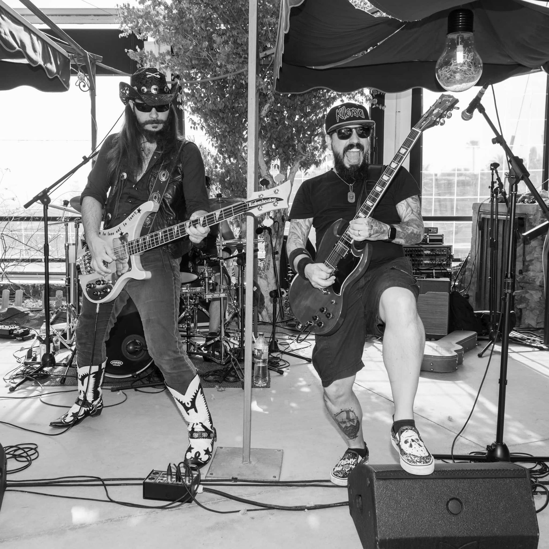 Two men are playing guitars on a stage under an umbrella